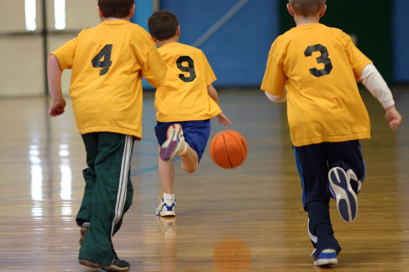 Bambini che giocano a basket in palestra, maglie numerate.